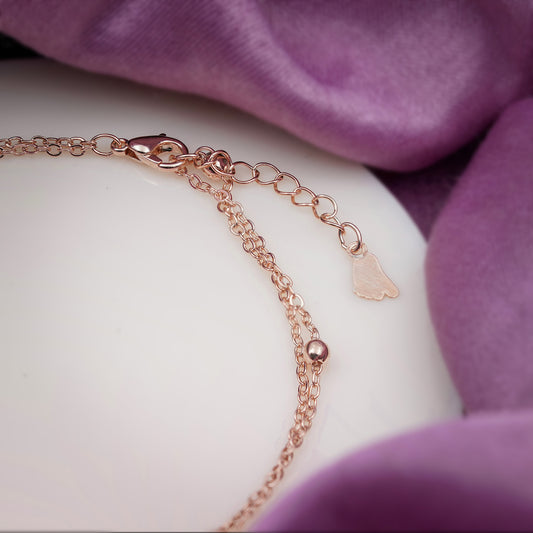 Rose gold anklet with heart clasp and small petal-shaped charm dangle