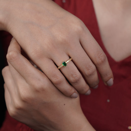 Gold ring with emerald green solitaire and pavé band on a hand