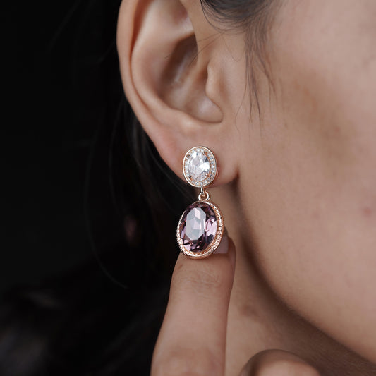 Rose gold drop earrings on ear: oval purple stone with clear halo and stud top