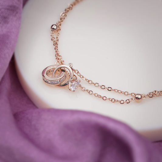 Rose-gold anklet charm with heart-and-loop design and small clear stone on chain