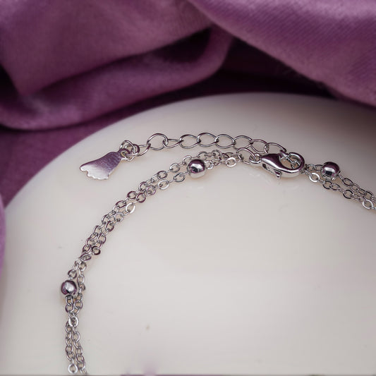 Women’s stainless steel anklet on display with zigzag charm, beads, and small wing tag
