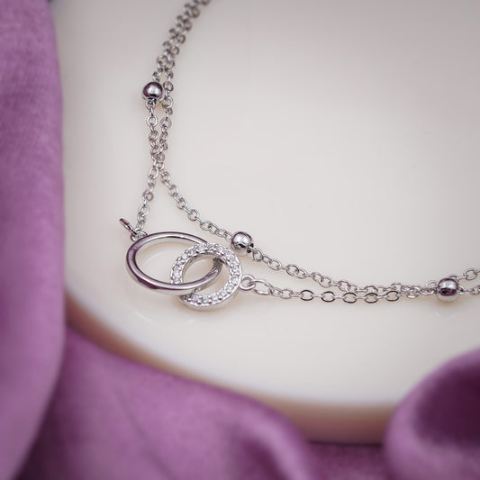 Silver-tone anklet detail with oval-and-circle pendant and small stone bezel