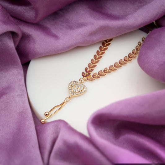Gold leaf-link heart CZ tassel pendant necklace on purple fabric, side angle.