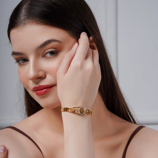 Gold-tone heritage motif bangle with round medallion at the center on wrist