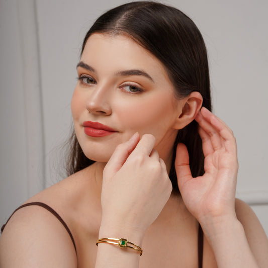 Gold bracelet cuff kada with emerald green square stone, on wrist near hand