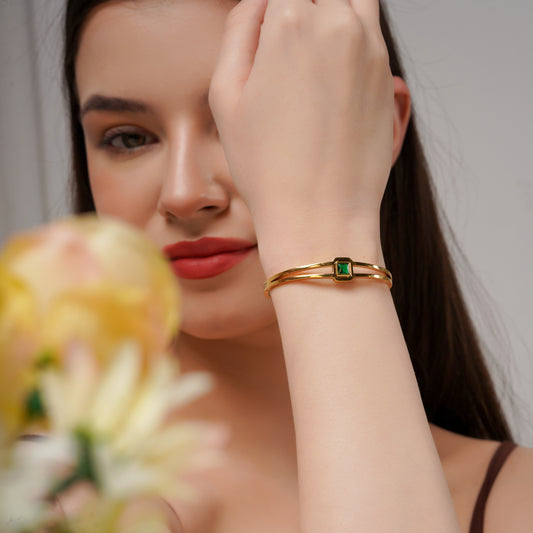 Gold double-band cuff kada with emerald green square stone, worn on wrist
