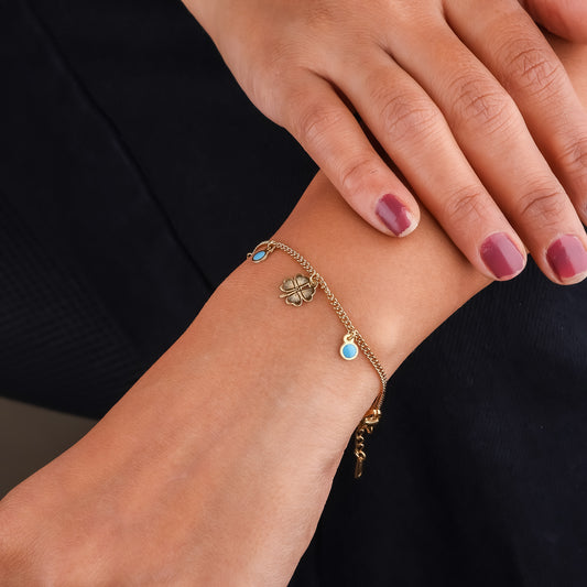 Gold-tone charm bracelet on wrist with clover charms and blue enamel round beads
